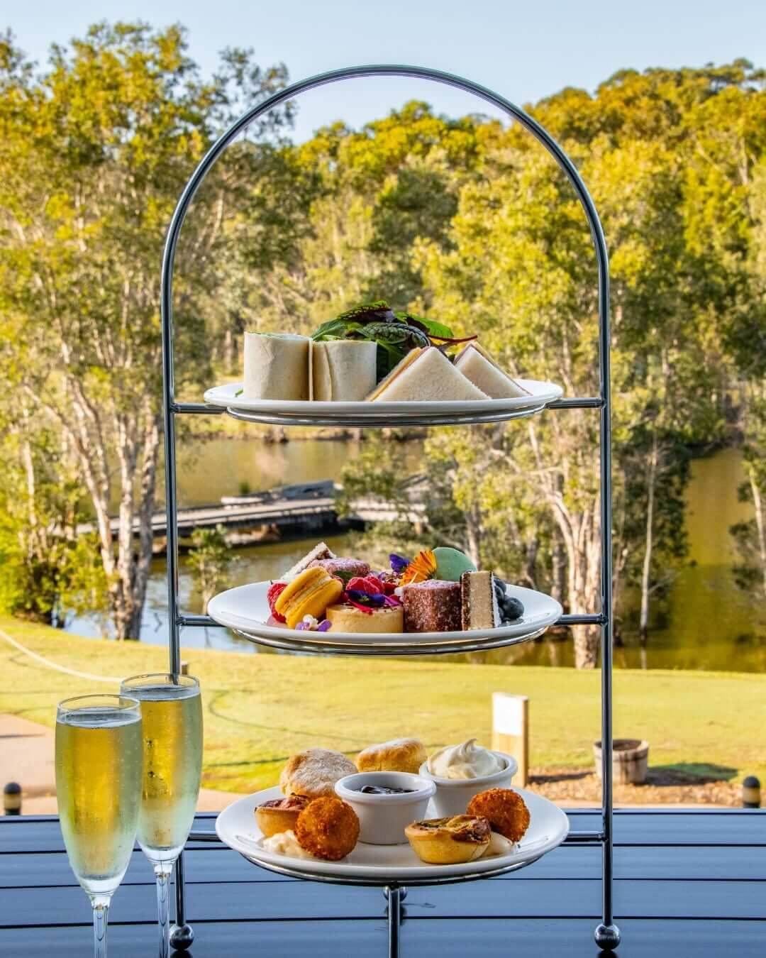 A three-tiered platter filled with sandwiches and pastries with two glasses of wine